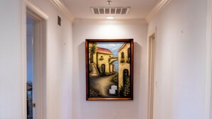 A hallway with a painting on the wall, carpeted floor, and white walls. - Santellan Manor (Paso Robles)