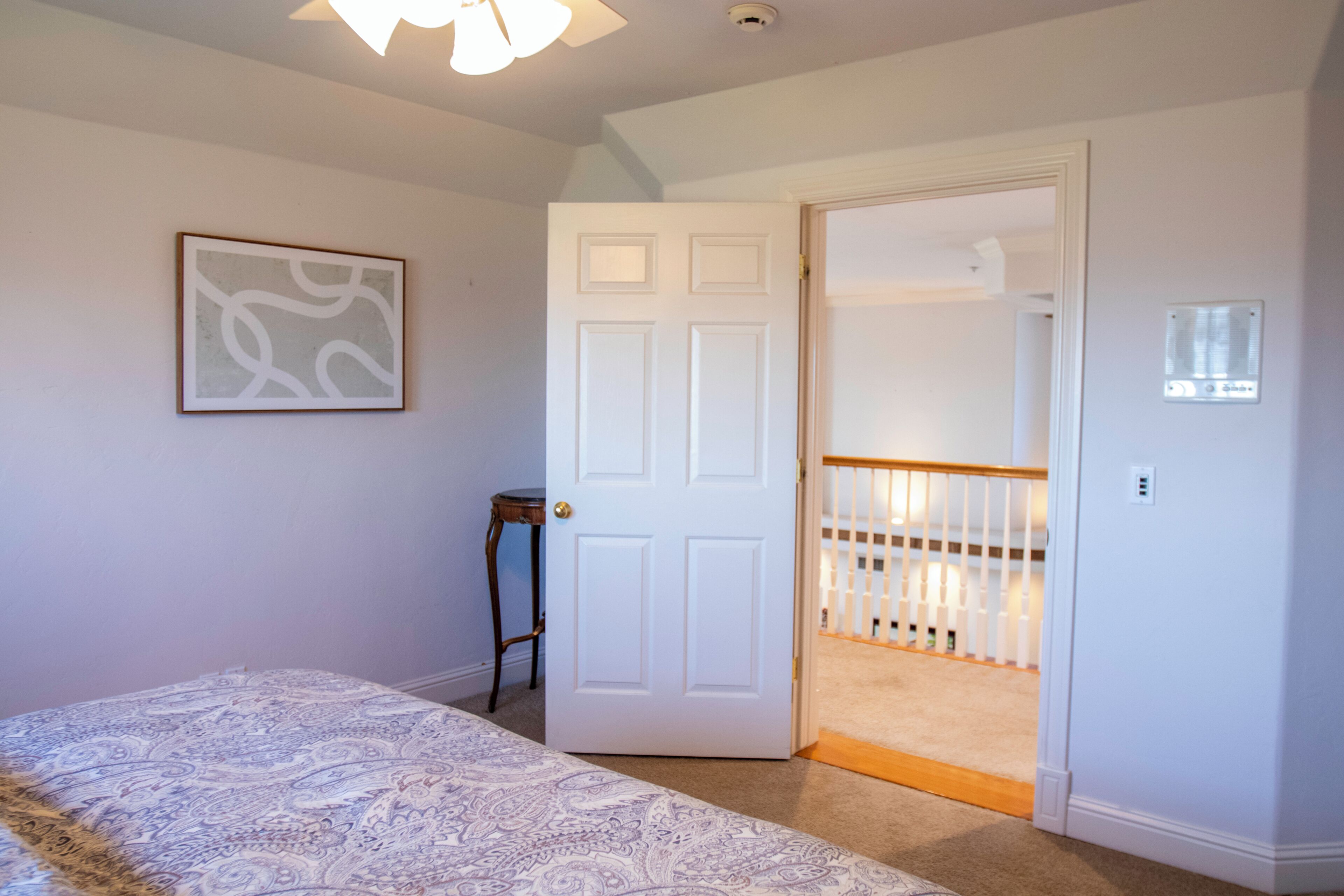 A bedroom with a bed, a door leading to a staircase, and a wall-mounted light fixture.