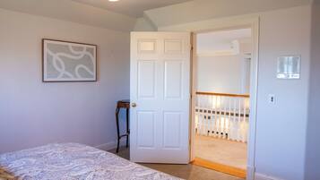 A bedroom with a bed, a door leading to a staircase, and a wall-mounted light fixture.