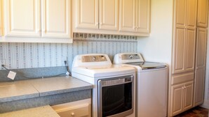 A laundry area with two white appliances, a countertop, and patterned wallpaper. - Santellan Manor (Paso Robles)