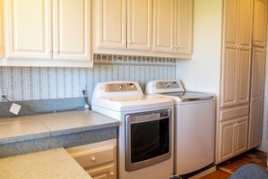 A laundry area with two white appliances, a countertop, and patterned wallpaper. - Santellan Manor (Paso Robles)