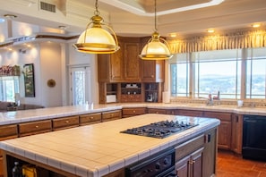 A spacious kitchen with a large island, wooden cabinets, and pendant lighting. - Santellan Manor (Paso Robles)