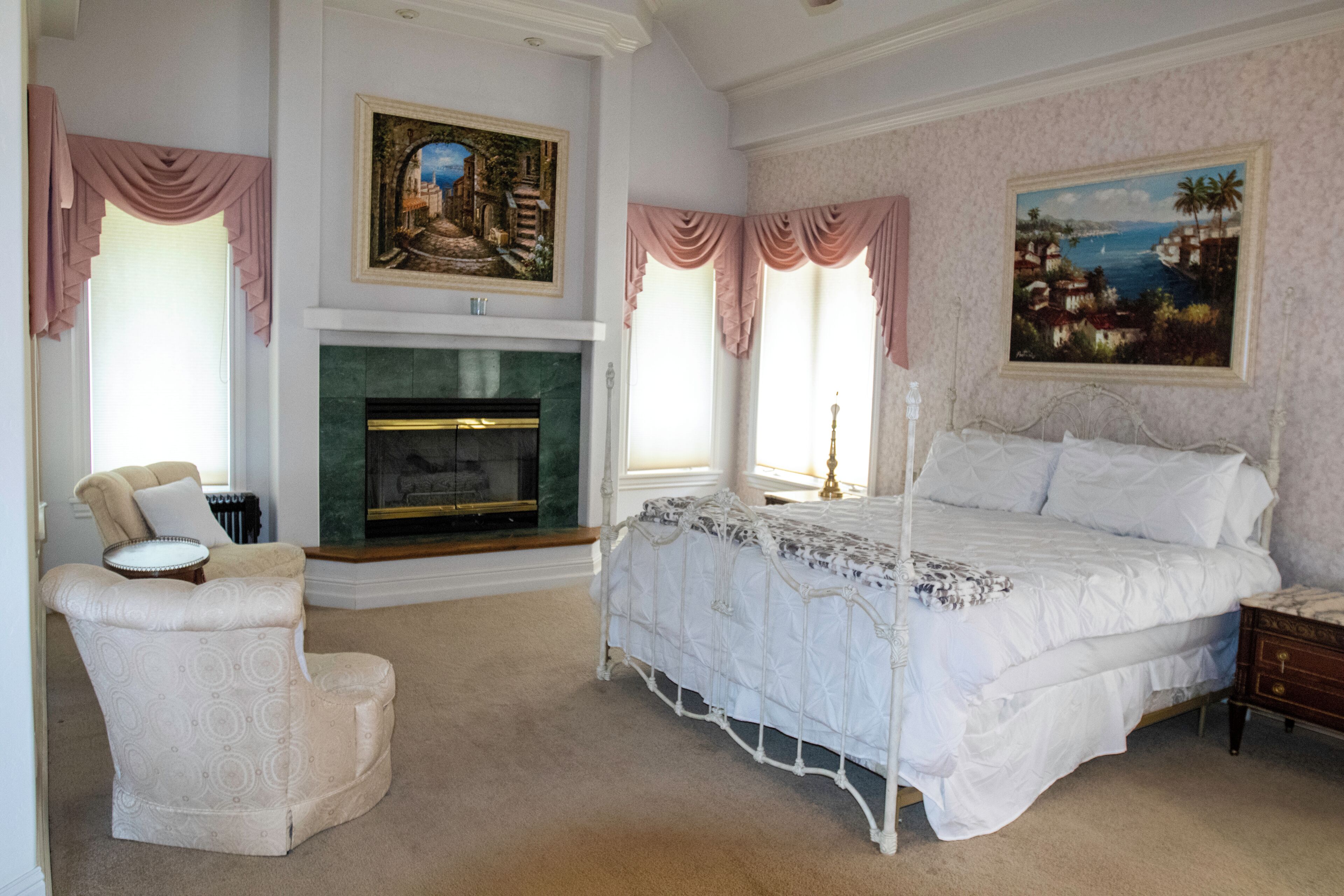 Une chambre à coucher avec un lit à baldaquin, une cheminée, un fauteuil et deux tableaux accrochés aux murs.