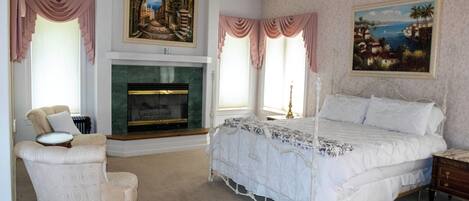 A bedroom with a four-poster bed, a fireplace, a chair, and two paintings on the walls.