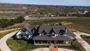 A large, two-story house with a stone chimney, surrounded by a well-maintained lawn and a driveway leading to a gated entrance. - Santellan Manor (Paso Robles)