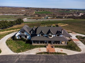 A large, two-story house with a stone chimney, surrounded by a well-maintained lawn and a driveway leading to a gated entrance. - Santellan Manor (Paso Robles)