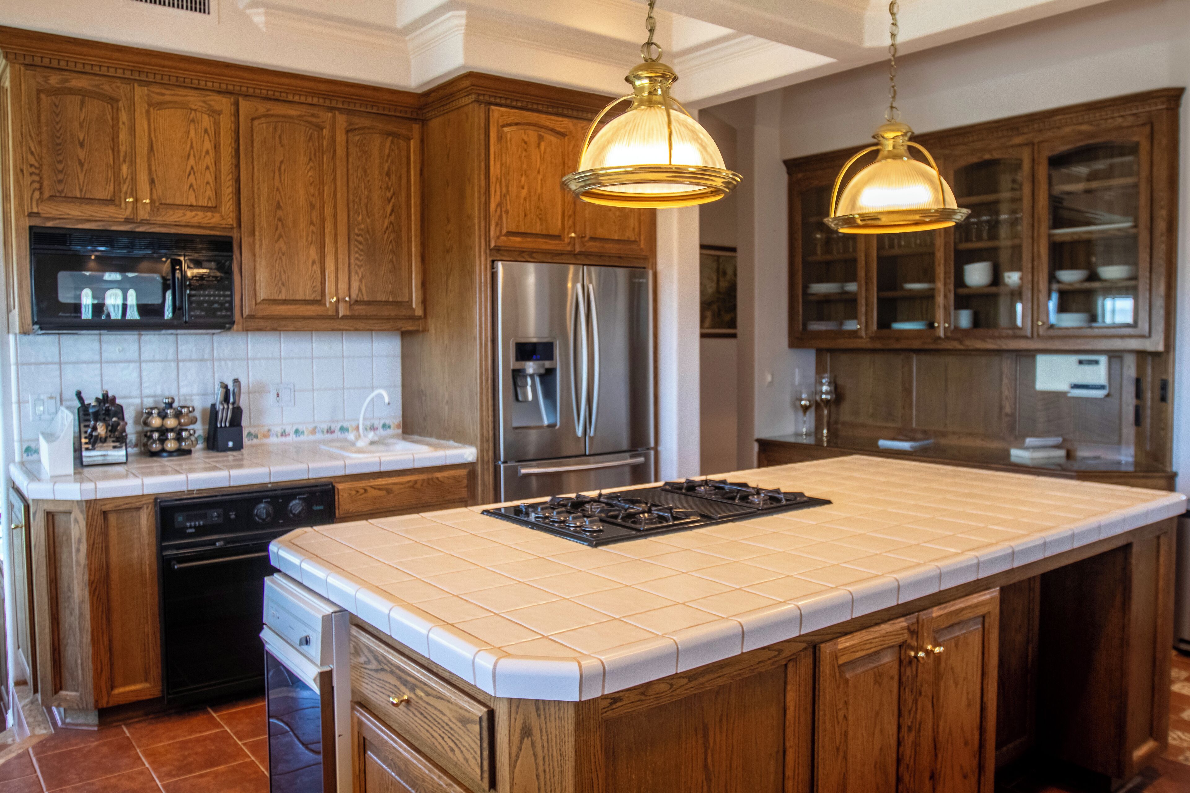 A kitchen with wooden cabinets, a stainless steel refrigerator, a built-in oven, and a large island with a gas stove.