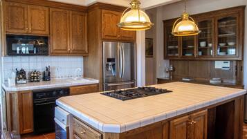 A kitchen with wooden cabinets, a stainless steel refrigerator, a built-in oven, and a large island with a gas stove.