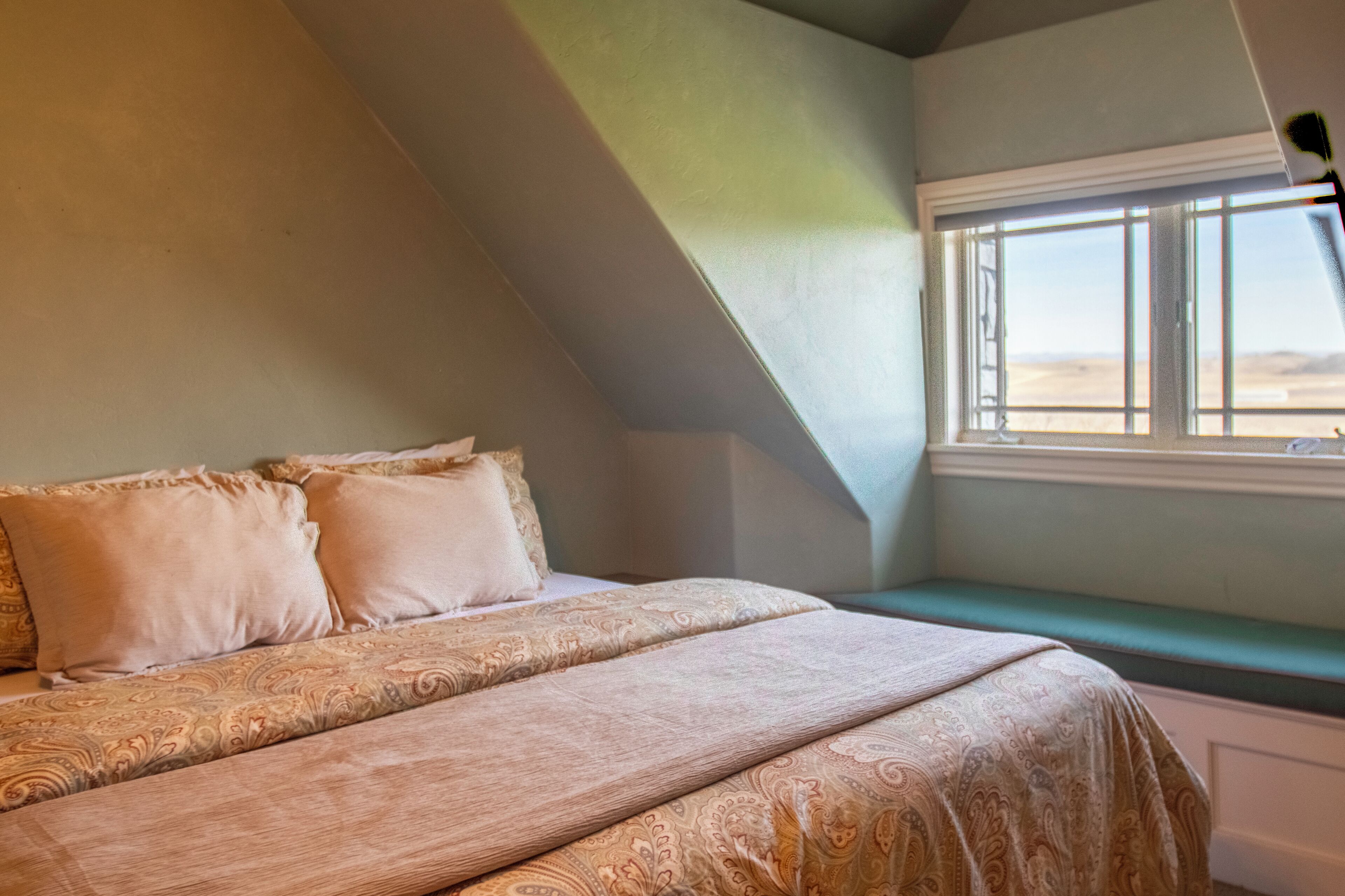 A bedroom with a bed, pillows, a window, and a sloped ceiling.