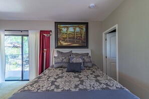 Um quarto com cama, quadro acima da cama, porta e vista através de uma porta de vidro.