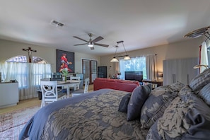 A bedroom with a large bed, a ceiling fan, a TV, and a dining area with a table and chairs. - San Antonio Estate (Atascadero)