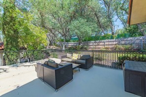 An outdoor patio area with wicker furniture, a metal fence, and trees in the background. - San Antonio Estate (Atascadero)