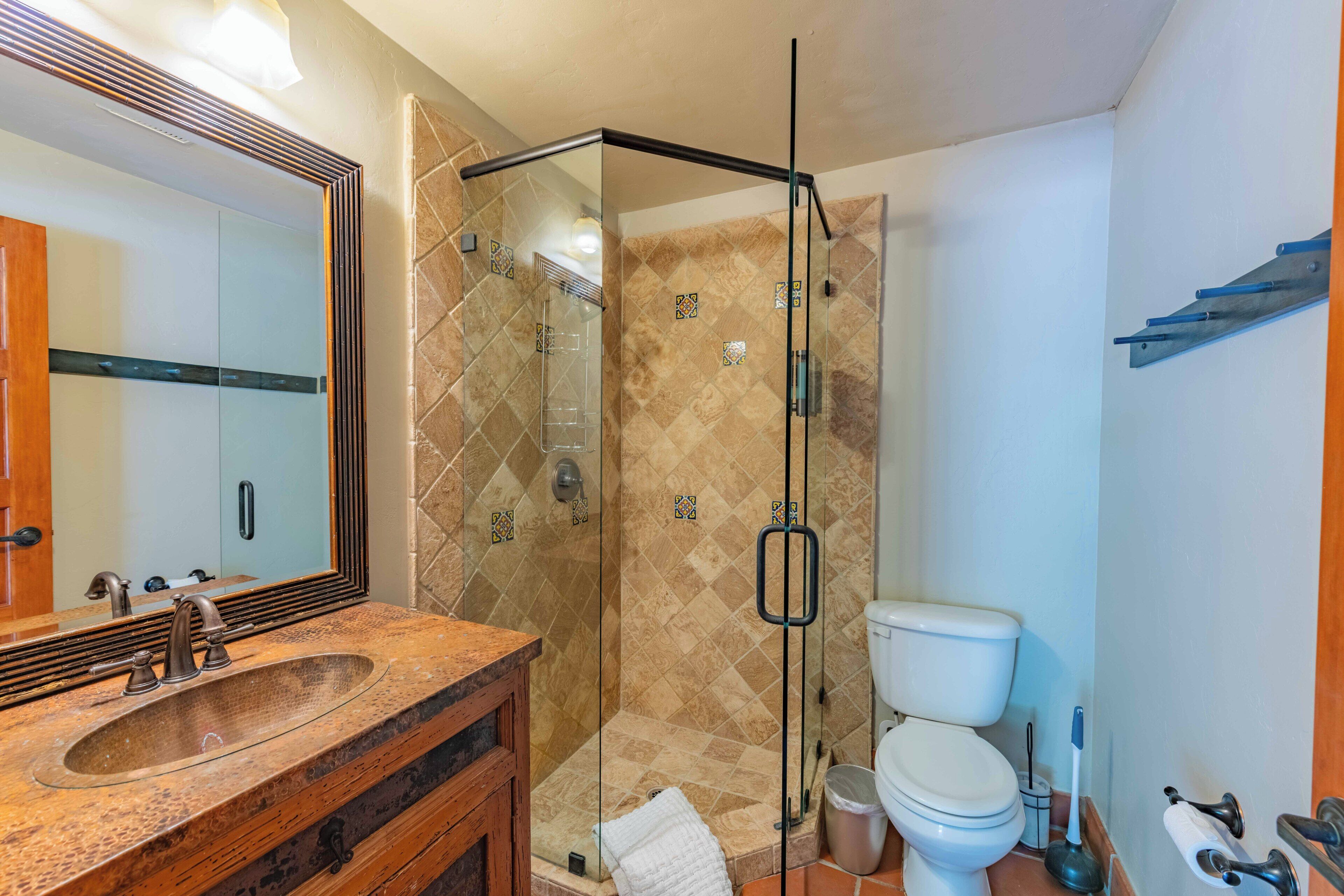 A bathroom with a glass-enclosed shower, a sink with a wooden vanity, and a toilet.