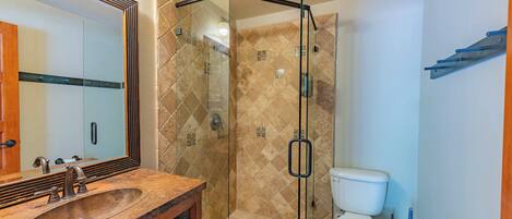 A bathroom with a glass-enclosed shower, a sink with a wooden vanity, and a toilet.