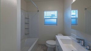 A bathroom with a bathtub, toilet, and a large mirror. There are two windows with blinds. - Park Street Apartment - Front Unit (Paso Robles)