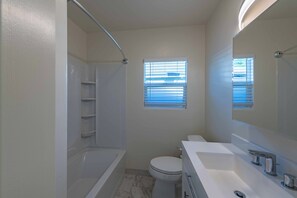A bathroom with a bathtub, toilet, and a large mirror. There are two windows with blinds. - Park Street Apartment - Front Unit (Paso Robles)