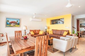 A modern living room with a wooden dining table, brown sofas with yellow cushions, and a yellow accent wall. - 3br 6 Guests  Ocean view private pool (Sánchez)