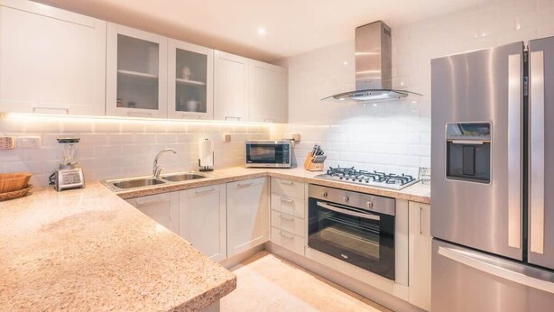Una cocina moderna con armarios blancos, encimera de granito, microondas integrado, estufa a gas y refrigerador de acero inoxidable.