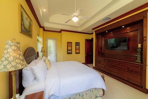 Une chambre d’hôtel avec un lit, un ventilateur de plafond, une télévision et une commode en bois.