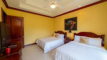 Habitación de hotel con dos camas, un ventilador de techo, un cuadro de un loro y un televisor sobre un mueble de madera.