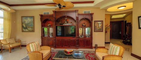A spacious living room with a large wooden entertainment center, comfortable seating, and a ceiling fan.