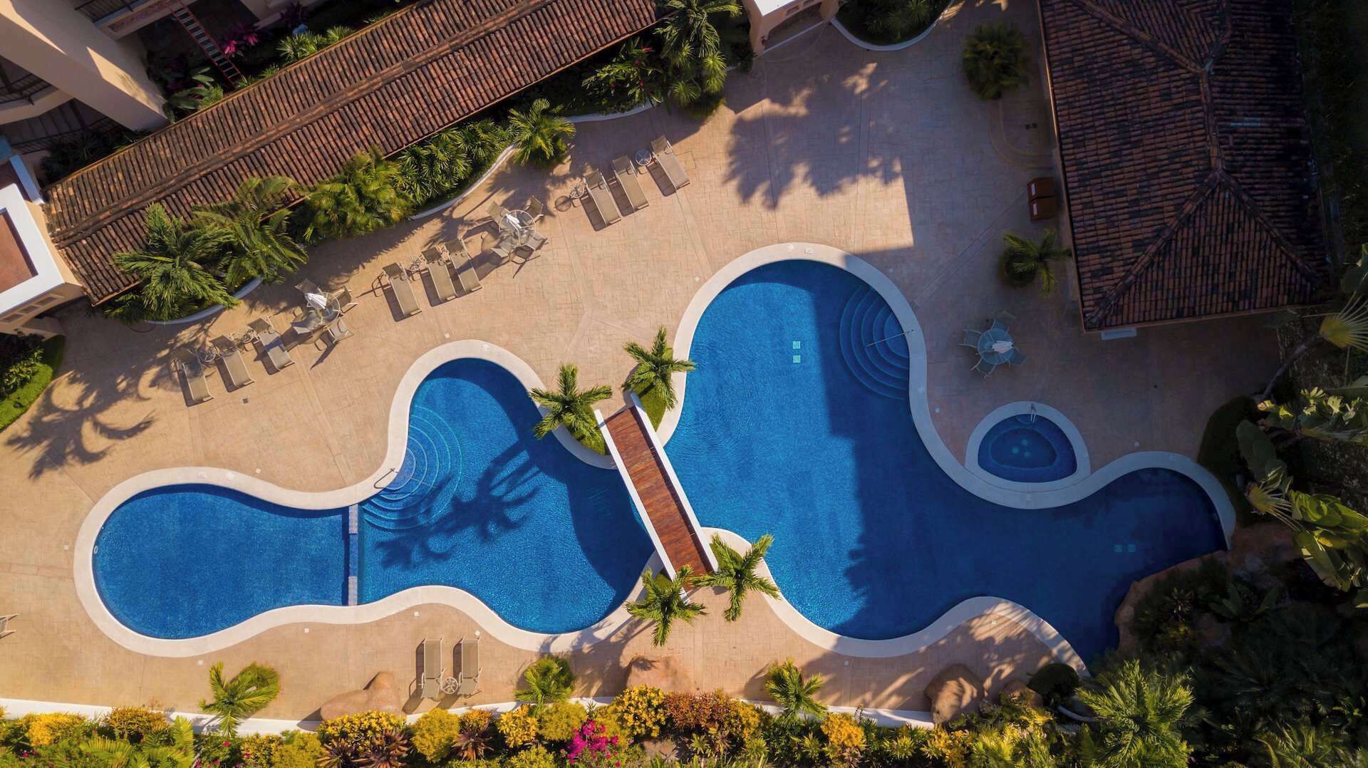 Vista aérea de un complejo turístico con varias piscinas, palmeras y áreas de descanso.