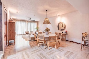 Un salon spacieux avec une table de salle à manger ronde, des chaises en bois, un luminaire suspendu en rotin et un ventilateur de plafond.