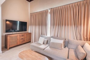 A living room with a flat-screen TV, wooden cabinet, beige sofa, and curtains. - Apartment w 3br near the beach in Portillo Raa (Las Terrenas)
