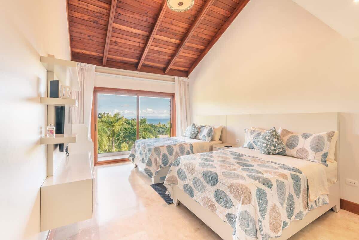 Une chambre avec deux lits, un plafond en bois, une grande fenêtre donnant sur un beau paysage et une petite table de chevet.