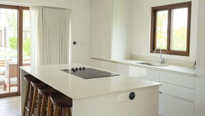 Una cocina moderna con una isla central, taburetes de bar, un ventanal grande y una lámpara colgante.