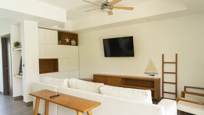 Una sala de estar moderna con un sofá blanco, una mesa de centro de madera y un televisor montado en la pared.
