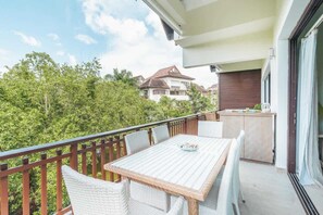 En balkon med bord og stole, en skydedør samt udsigt til nabohuse og træer.