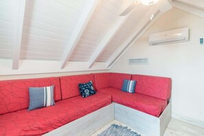 Ein rotes Ecksofa mit gemusterten Kissen, eine weiße Decke mit Dachfenstern und eine Wand-Klimaanlage.