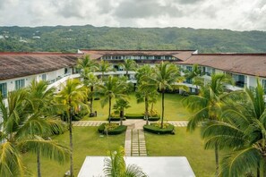 A hotel courtyard with a central lawn, palm trees, and a building with a red roof.