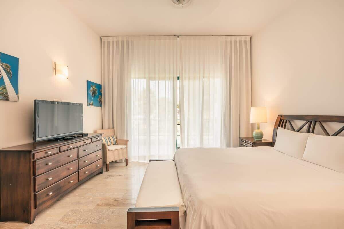Une chambre d’hôtel avec un lit, un téléviseur posé sur une commode en bois, une lampe et une fenêtre avec des rideaux.