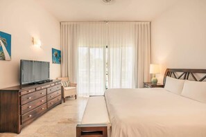 A hotel room with a bed, a TV on a wooden dresser, a lamp, and a window with curtains.