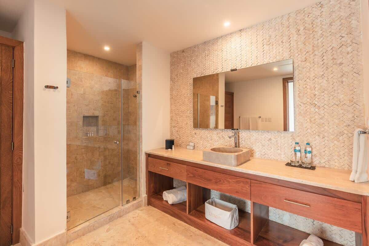 Une salle de bain moderne dotée d’une douche à parois de verre, d’un grand miroir et d’un meuble-lavabo en bois avec des tiroirs de rangement.