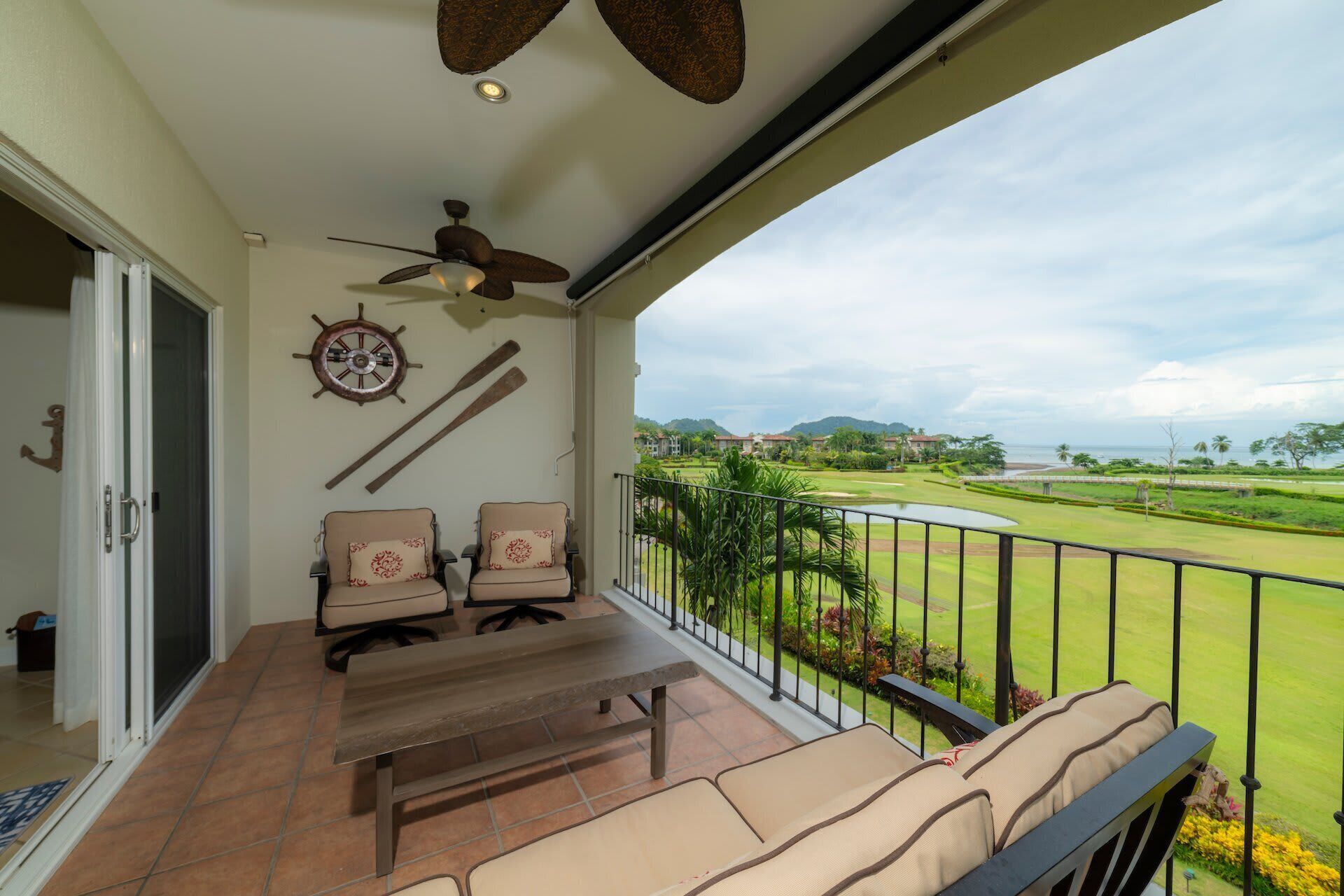 Un balcon avec une table et des chaises, un ventilateur de plafond, un gouvernail de bateau et une vue sur un terrain de golf.