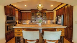 A kitchen with wooden cabinets, a large island with bar stools, stainless steel appliances, and a decorative light fixture. - Montebello 4E 3bed 3 bath (Jacó)