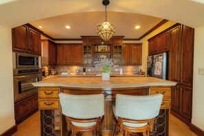 A kitchen with wooden cabinets, a large island with bar stools, stainless steel appliances, and a decorative light fixture. - Montebello 4E 3bed 3 bath (Jacó)