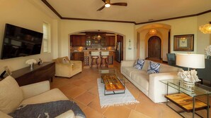 A spacious living room with a television, sofas, a coffee table, and a ceiling fan. - Montebello 4E 3bed 3 bath (Jacó)