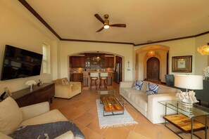 A spacious living room with a television, sofas, a coffee table, and a ceiling fan. - Montebello 4E 3bed 3 bath (Jacó)