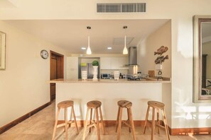 A modern kitchen with a central island, wooden stools, pendant lighting, and a visible clock. - Puerto Bahia Villa Pool, BBQ & Amazing views! (Sánchez)