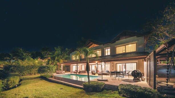 Ein zweistöckiges Haus mit Pool, Sitzgelegenheiten im Freien und einer überdachten Terrasse.