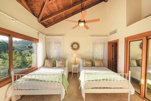A bedroom with two beds, a ceiling fan, a nightstand with a lamp, and a view of the outdoors. - Puerto Bahia Villa Pool, BBQ & Amazing views! (Sánchez)