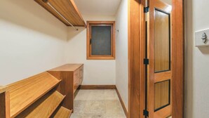 Ein schmaler Korridor mit Holzboden, einem kleinen Fenster, einer hölzernen Sitzbank und einer Tür mit schwarzem Griff.