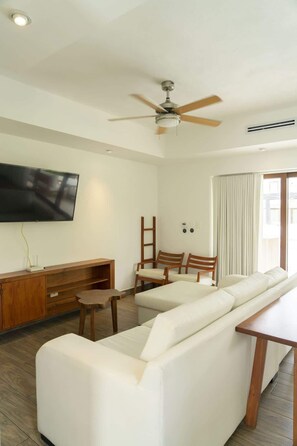 A modern living room with a flat-screen TV, wooden furniture, a ceiling fan, and large windows. - Villa with direct pool access in gathered complex (Monterrico)