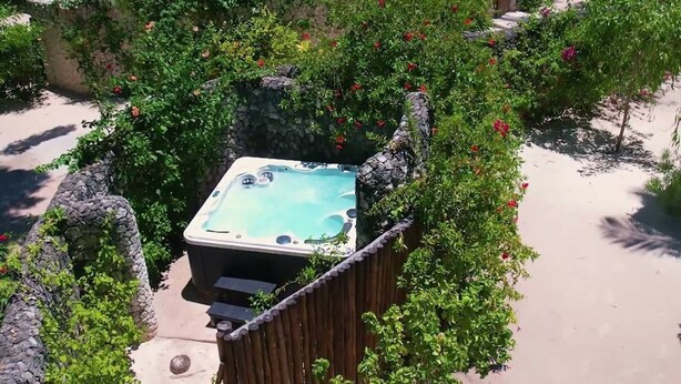 A hot tub surrounded by lush greenery and a stone wall. - Classic Deluxe Retreat (Paje)