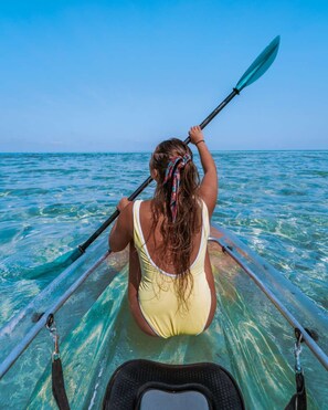 Eine Person in einem gelben Badeanzug rudert mit einem Kajak auf klarem türkisblauem Wasser.