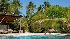 A pool area with lounge chairs, a covered seating area, and lush tropical vegetation. - Classic Deluxe Retreat (Paje)